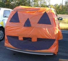 an orange and black pumpkin shaped tent sitting on the side of a road next to a white car