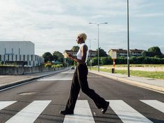 a woman is walking across the street with her cell phone in hand and she is wearing black pants