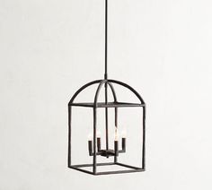 an iron caged light fixture with four lit candles in the center, hanging on a white wall