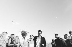 a group of people standing around each other in front of the ocean with drinks and confetti