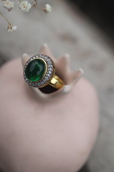 This elegant ring features a central green stone surrounded by sparkling cubic zirconia, adding a touch of glamour to any ensemble. Its versatility makes it perfect for complementing a variety of outfits and styles. Finish: 22KT Gold Plating Material: Silver, Copper Alloy, Polki Color: Green Size: One Size Closure Type: Adjustable Box Contains: 1 Ring Formal Crystal Diamond Ring With Stones, Formal Diamond Crystal Ring With Stones, Classic Green Diamond Crystal Ring, Classic Green Crystal Diamond Ring, Elegant Crystal Ring With Stones For Formal Occasions, Dazzling Green Diamond Ring For Formal Occasions, Green Diamond Rings With Pave Setting, Elegant Round Diamond Ring With Stones, Elegant Round Diamond Ring