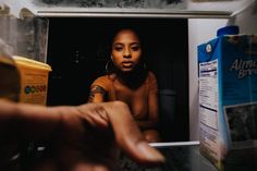 a woman is sitting in the microwave with her hand on the door and another person reaching for something