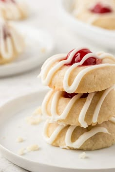 three cookies with white icing and cherry toppings on a plate next to another cookie