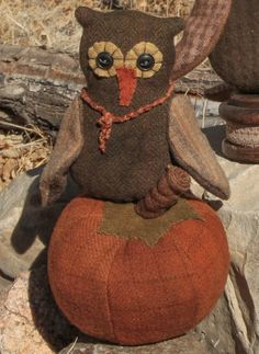 an owl stuffed animal sitting on top of a small pumpkin in front of some rocks