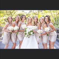 a group of women standing next to each other on a wooden bridge holding bouquets