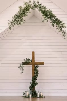 a cross and candles in front of a white wall with greenery growing on it