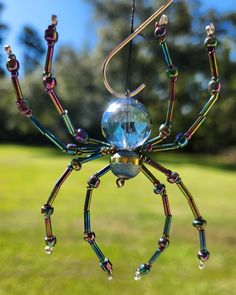 a spider made out of beads hanging from a string in the grass with trees in the background