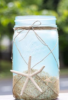 a blue mason jar filled with sand and starfish on top of a wooden table