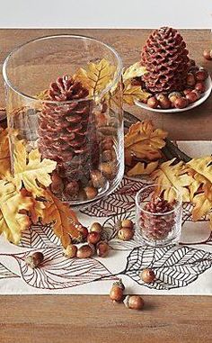 pine cones, acorns and leaves are arranged on a wooden table with glass dishes