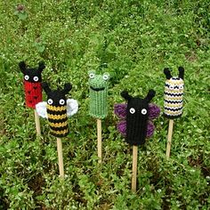 four little crocheted bugs sitting on top of wooden sticks in the green grass