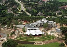 an aerial view of a large home surrounded by lush green trees and buildings in the background