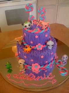 there is a purple cake decorated with littlest pet shop characters on top of it