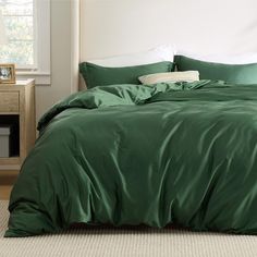 a bed with green sheets and pillows in a room next to a night stand on the floor