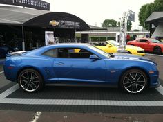 a blue chevrolet camaro is parked in front of a performance shop with other cars