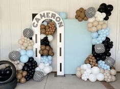 an arch made out of balloons and black and white checkered balloons is displayed in front of a blue door