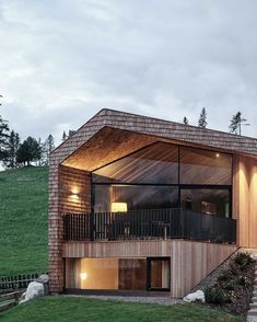 a wooden house on top of a grassy hill with stairs leading up to the second floor