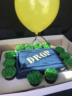 a cake in the shape of an arrow with green frosting and cupcakes