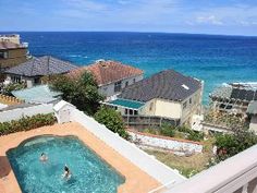 an outdoor hot tub overlooking the ocean and houses in the distance with people swimming in it