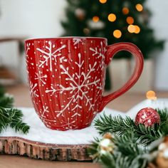 a red coffee cup sitting on top of a wooden table next to christmas tree branches