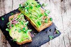 two pieces of bread topped with avocado and sprouts on a slate board