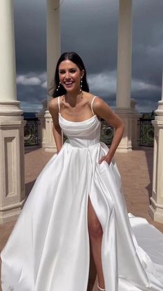 a woman wearing a white dress standing in front of pillars with her leg up on the ground