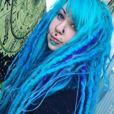 a woman with blue dreadlocks and piercings standing next to a skateboard