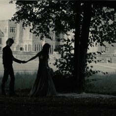 a man and woman holding hands in front of a tree