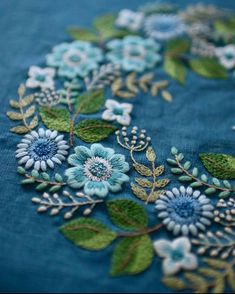 blue flowers and leaves are embroidered onto a piece of fabric with green leaves on it