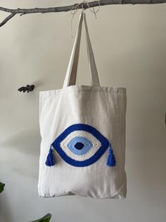 This blue evil eye boho tote bag made of Turkish Buldan cotton fabric with hidden pocket inside. Hand crocheted evil eye pattern is made of %100 cotton yarn. Hand crocheted evil eye sewn on a natural Turkish Buldan cotton fabric bag  with a sewing machine. Double layer cotton tote will be a great helper in your everyday use.Dimensions & Info:Width: 17 inches / Height 18.5 inches / Bottom depth 3.5 inches / Strap length  25.5 inchesTote bag has inside two pockets: 5x 7.5 inches / 3x7.5 inches Handmade Bohemian Cotton Beach Bag, Handmade Blue Cotton Bags, Handmade Blue Cotton Bag, Evil Eye Crochet Bag Pattern Free, Blue Bohemian Canvas Tote Bag, Blue Bohemian Tote Canvas Bag, Blue Eco-friendly Crochet Bag, Evil Eye Tote Bag, Evil Eye Pattern