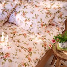 a bed with pink flowers on it and a wooden side table in front of it