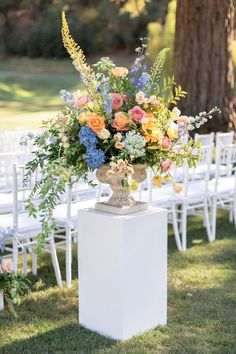 a vase filled with flowers sitting on top of a white pedestal next to an aisle