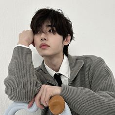 a young man wearing a sweater and tie leaning on a chair with his hand on his head