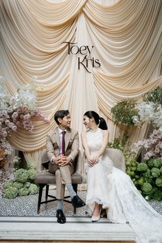 a man and woman sitting next to each other in front of a stage with flowers