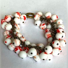 a close up of a bracelet on a white surface with red and white balls around it