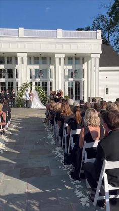 a wedding ceremony in front of a large white building with lots of people sitting on chairs