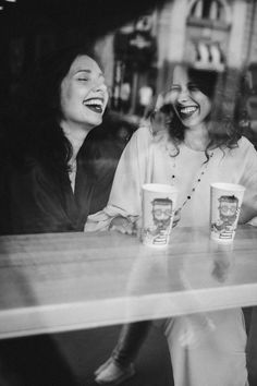 two women sitting at a table laughing and drinking coffee