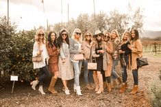 a group of women standing next to each other in front of an orange tree and bushes