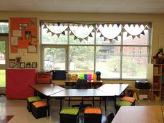 an empty classroom with tables and chairs in front of large windows that have bunting flags on them