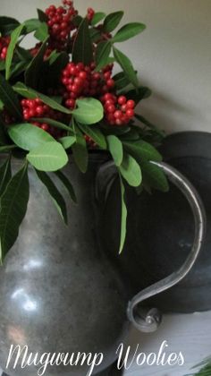 a metal pitcher filled with red berries and green leaves