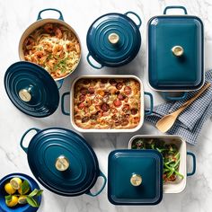 blue casserole dishes with lids and serving utensils on a marble table