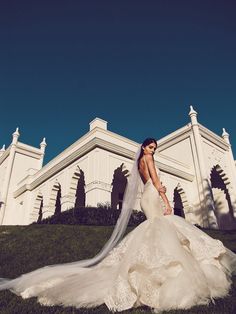 a woman in a wedding dress is posing for a photo on the grass near a building