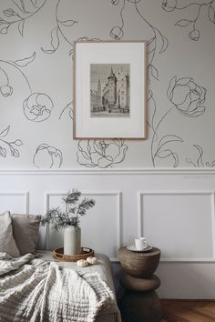 a bed sitting under a framed picture next to a wall with flowers and leaves on it