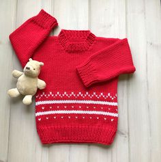 a teddy bear is sitting next to a red sweater and mittens on the floor