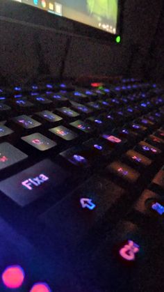 a close up of a keyboard with glowing lights on it's keys and the screen in the background