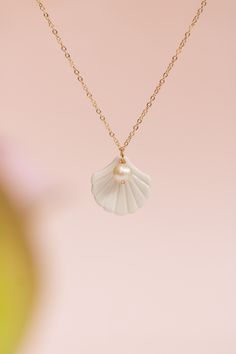 a necklace with a white shell hanging from it's center on a gold chain