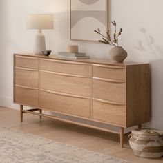 a wooden dresser sitting in a living room next to a lamp and painting on the wall