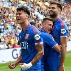 three soccer players are standing together in front of a crowd and one has his mouth open