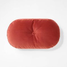 an orange round pillow on a white surface with a button in the middle and a small hole at the bottom