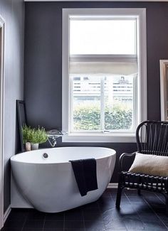 a white bath tub sitting under a window next to a chair in a room with gray walls