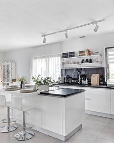 a white kitchen with black counter tops and stools in front of the sink area